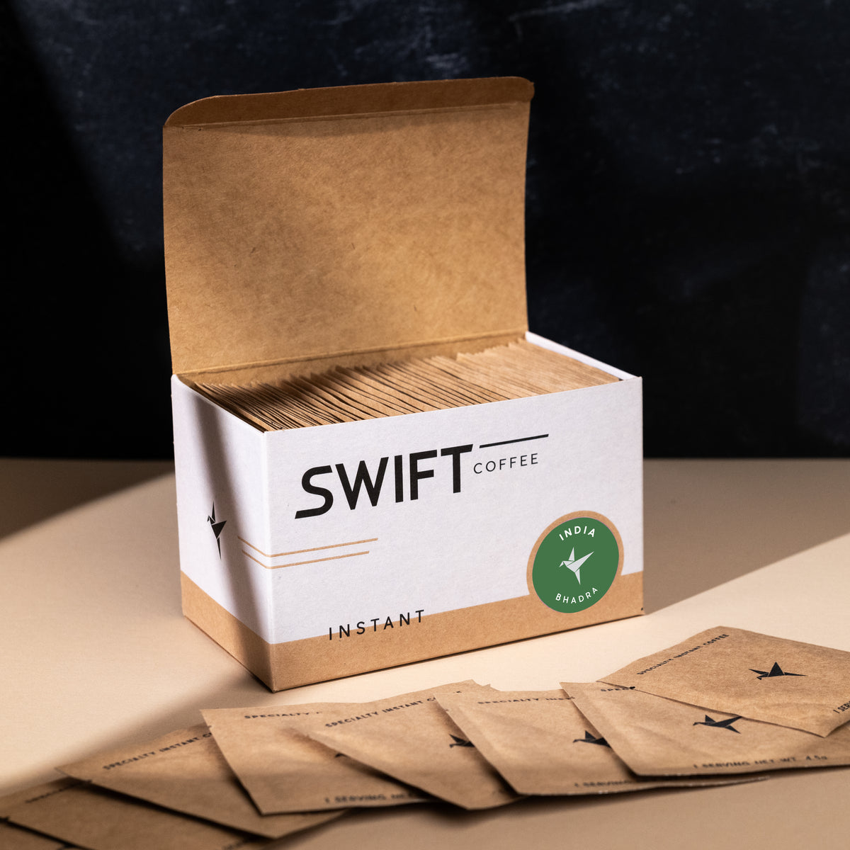 Open box of Swift Coffee India Bhadra single-serve sachets with loose sachets spread in front, on a dark backdrop