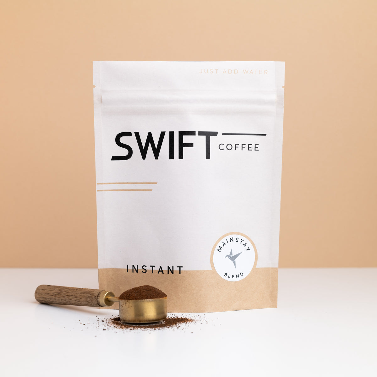 Swift Coffee Mainstay Blend instant coffee bulk pouch with a brass scoop of instant coffee in front
