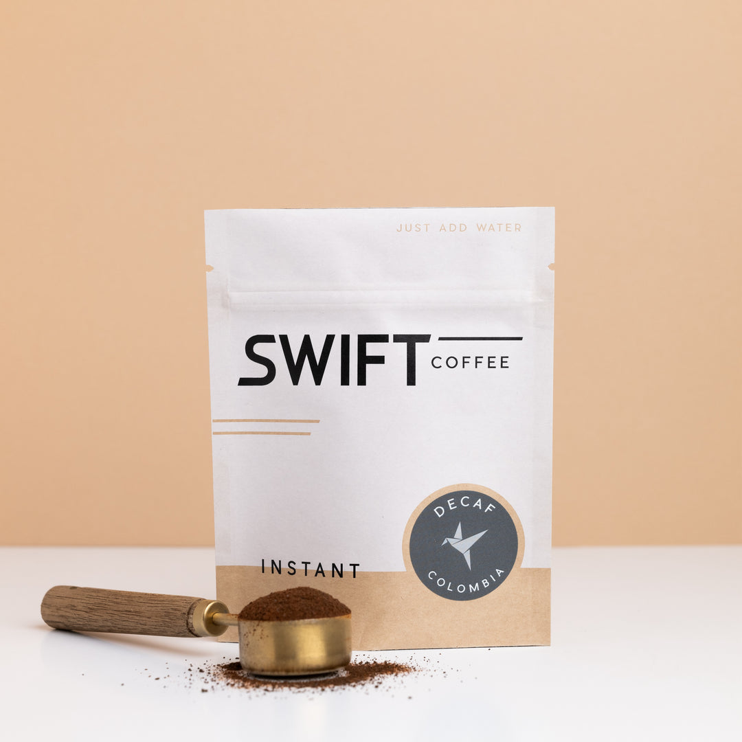 Swift Coffee Decaf Colombia instant coffee bulk pouch with a brass scoop of instant coffee in front