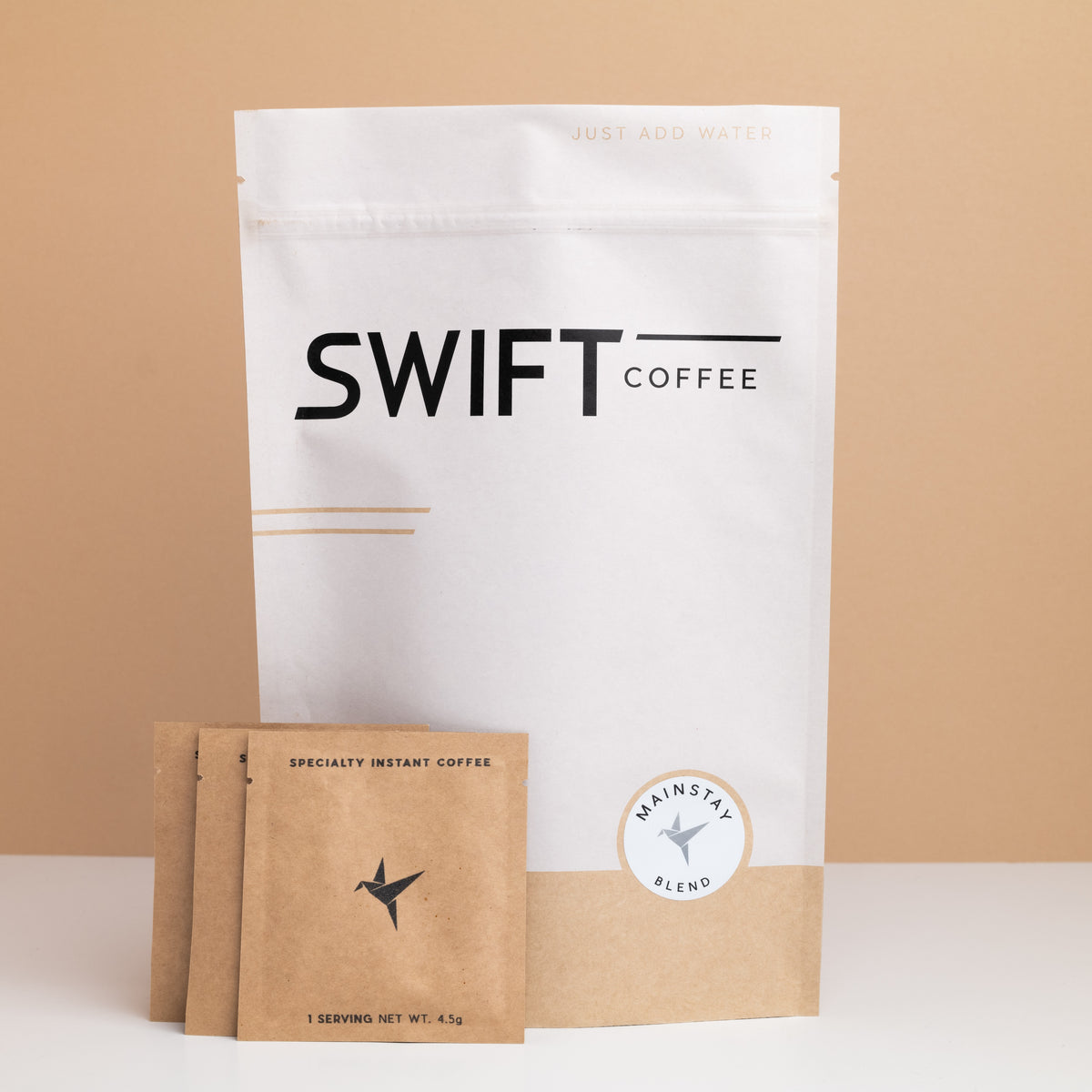 Swift Coffee Mainstay Blend instant coffee pouch with a stack of kraft single-serve sachets