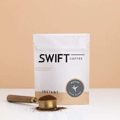 Swift Coffee Decaf Latin Blend instant coffee pouch with a brass scoop of instant coffee in front