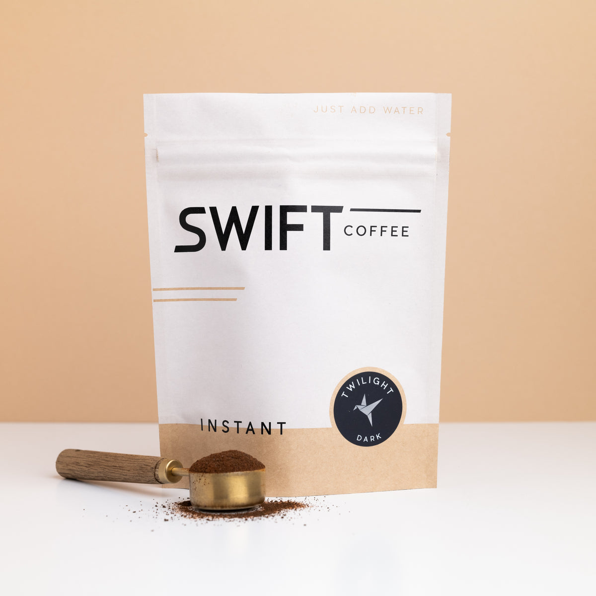 Swift Coffee Twilight Dark Roast instant coffee pouch with a brass scoop of instant coffee in front