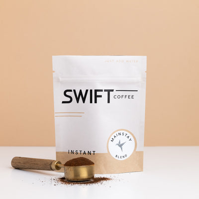 Swift Coffee Mainstay Blend instant coffee pouch with a brass scoop of instant coffee in front