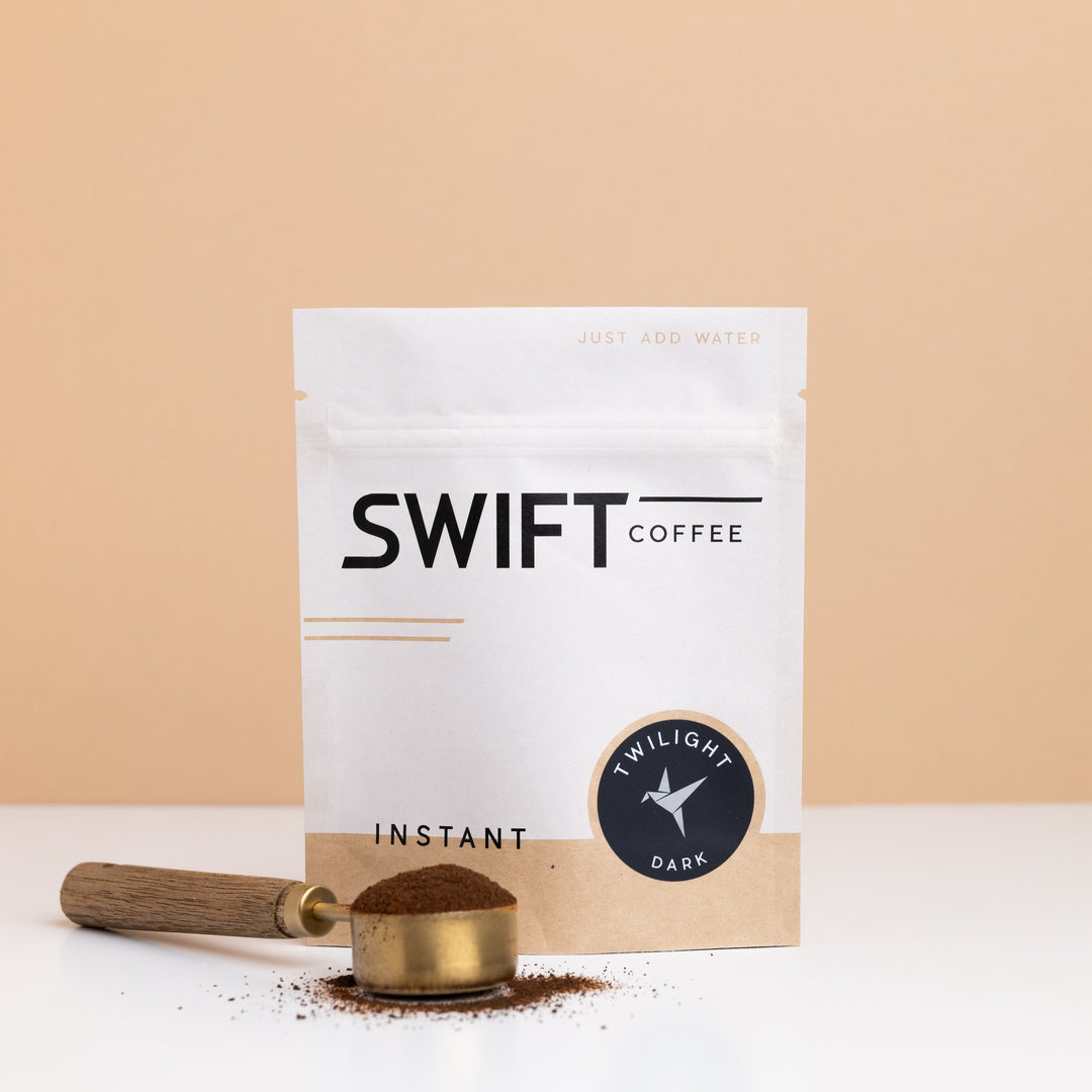 Swift Coffee Twilight Dark Roast instant coffee bulk pouch with a brass scoop of instant coffee in front