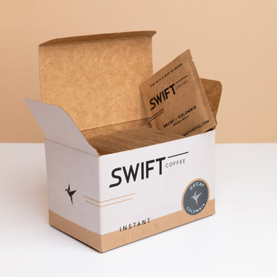 Open box of Swift Coffee Decaf Colombia instant coffee single-serve sachets with one sachet propped on top