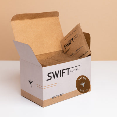 Open box of Swift Coffee Brazil Bom Dia instant coffee single-serve sachets with one sachet propped on top