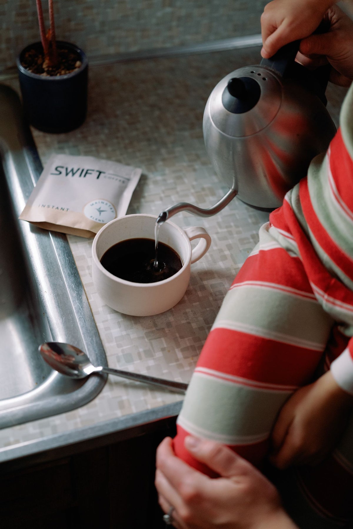Pouring hot water into a mug of Swift instant coffee at the kitchen counter