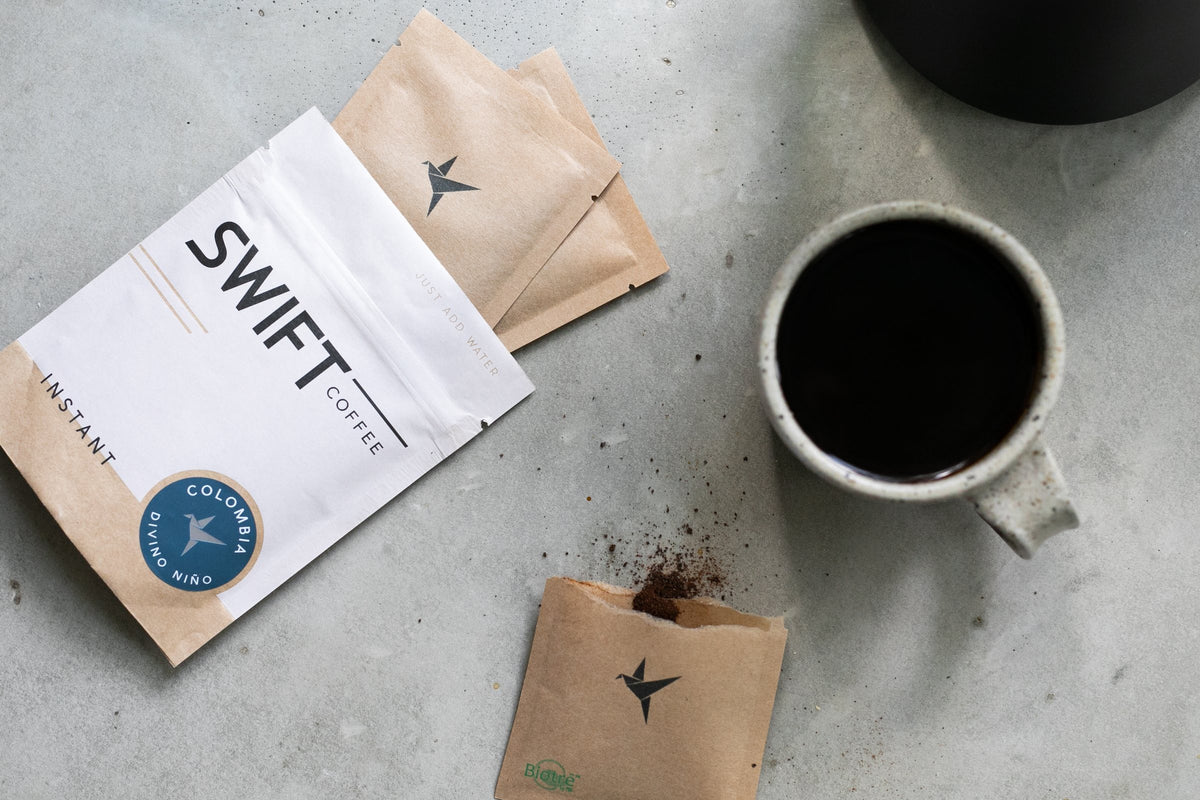 Overhead view of a Swift Coffee pouch, kraft single-serve sachets and a mug of black coffee on a concrete counter