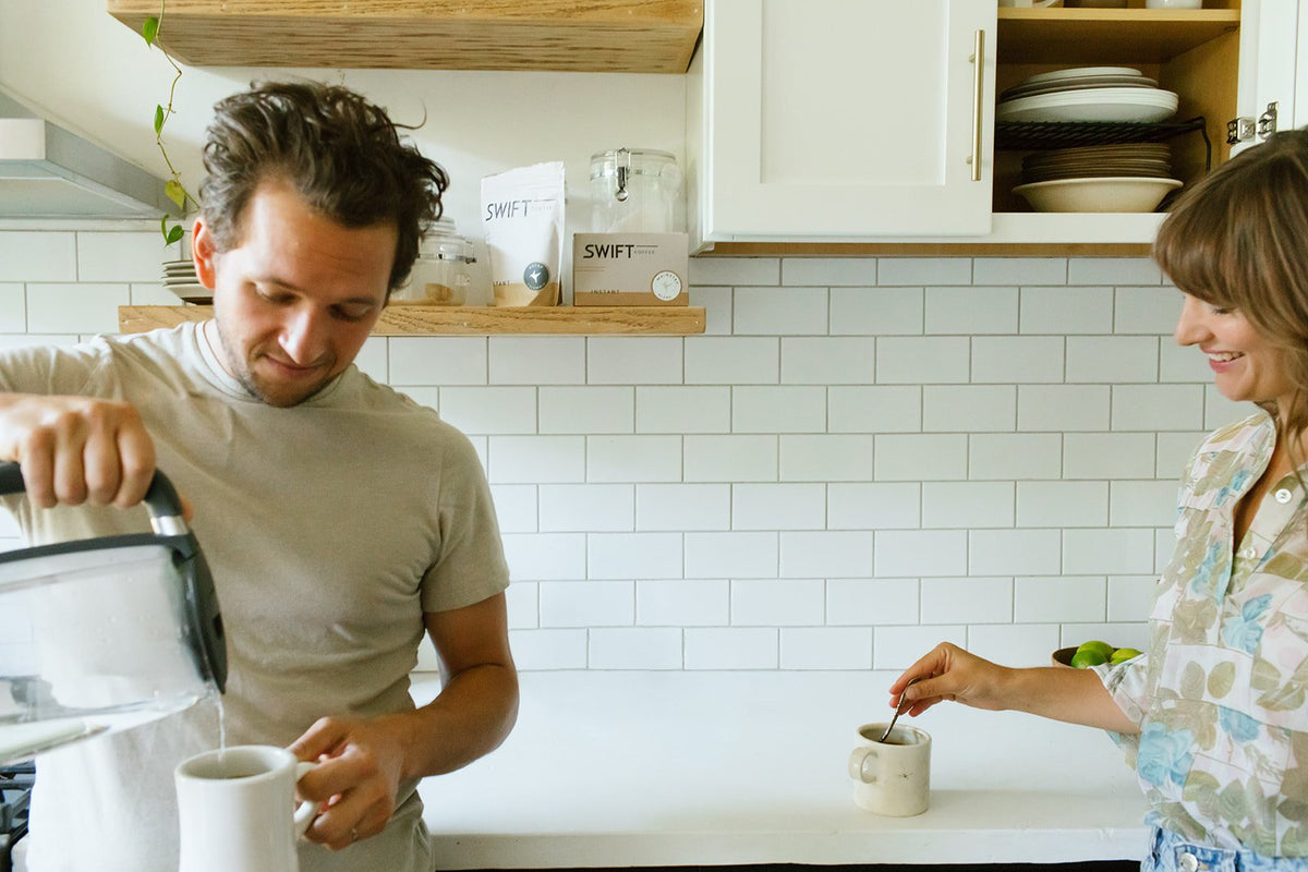 Two people making Swift Coffee together in a bright kitchen with white tile and open shelves