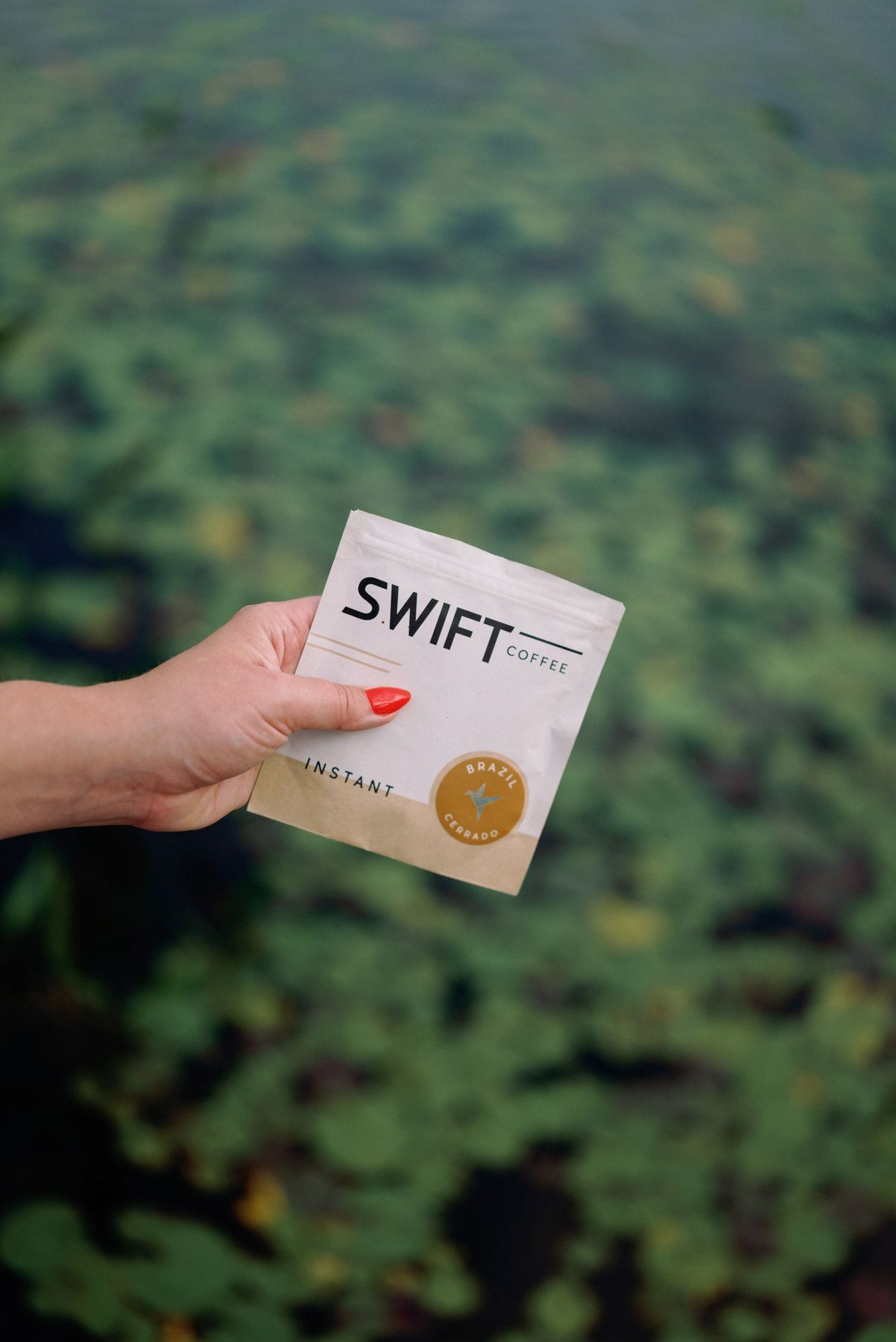 Hand holding a Swift Coffee pouch over a lily pond